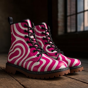 May include: A pair of pink and white patterned combat boots with black laces and a brown sole. The boots have a unique wavy design and are displayed on a wooden surface.