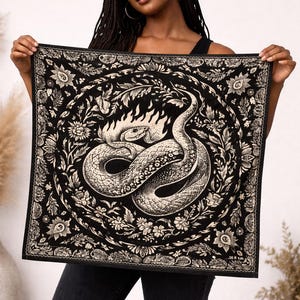 Puede incluir: Pañuelo cuadrado en blanco y negro con una ilustración detallada de una serpiente con llamas, rodeada de elementos florales y botánicos. El pañuelo se sostiene, mostrando el intrincado diseño y patrón.