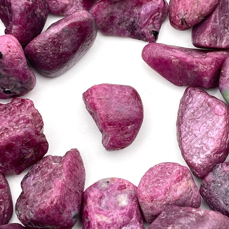 Peut inclure: Plusieurs pierres pr&eacute;cieuses de rubis brutes, non taill&eacute;es. Les pierres, de tailles et formes vari&eacute;es, pr&eacute;sentent une couleur rouge intense avec des nuances. La texture brute et les formes naturelles des rubis sont visibles sur fond blanc.