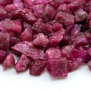 Peut inclure: Un tas de pierres précieuses rubis brutes. Les pierres sont d'un rouge profond et riche, avec un aspect légèrement translucide. Les pierres précieuses sont de forme irrégulière et de tailles variables, avec une texture brute et naturelle. Le fond est blanc.