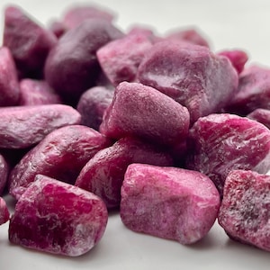 Peut inclure: Gros plan sur un tas de pierres pr&eacute;cieuses rubis brutes. Les pierres, de tailles et de formes vari&eacute;es, pr&eacute;sentent une teinte rouge-rose profond. Les pierres pr&eacute;cieuses ont un aspect naturel, non poli, avec des textures et des facettes visibles.