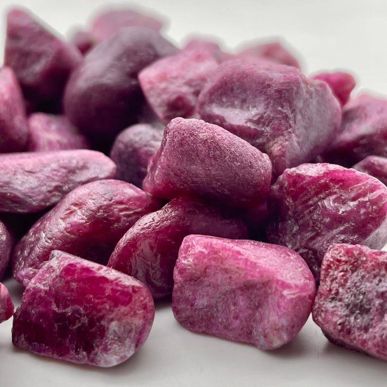 Peut inclure: Gros plan sur un tas de pierres pr&eacute;cieuses rubis brutes. Les pierres, de tailles et de formes vari&eacute;es, pr&eacute;sentent une teinte rouge-rose profond. Les pierres pr&eacute;cieuses ont un aspect naturel, non poli, avec des textures et des facettes visibles.