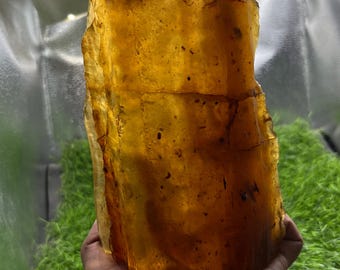 May include: A large, translucent, golden-yellow piece of raw amber with a rough, irregular texture. The stone features visible internal inclusions, natural fractures, and varying shades of honey and orange throughout its solid, crystalline structure.