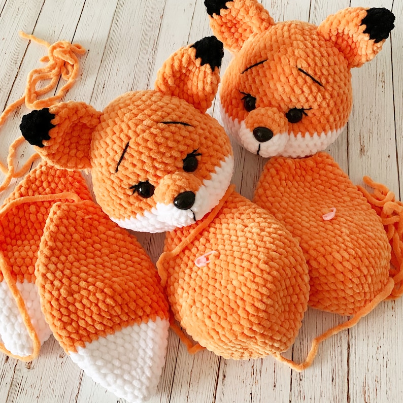 Op de afbeelding: Twee oranje gehaakte vos knuffels met witte accenten. De vossen hebben zwarte ogen en neuzen. De grotere vos heeft een lange, gekrulde staart.