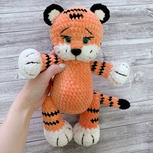 May include: A crocheted orange and black tiger plush toy with white accents. The toy has green eyes and a black nose.