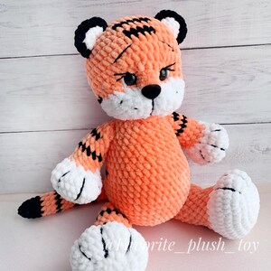 May include: A crocheted orange and black tiger plush toy with white accents. The toy has a black nose and black eyes.