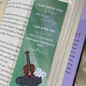 May include: A green bookmark with a black cat and a violin. The bookmark has the text "I can offer you my life but it is a short life. I can offer you my heart though I have no idea how many more beats it shall sustain." The bookmark also has the text "Jem Carstairs" at the bottom.