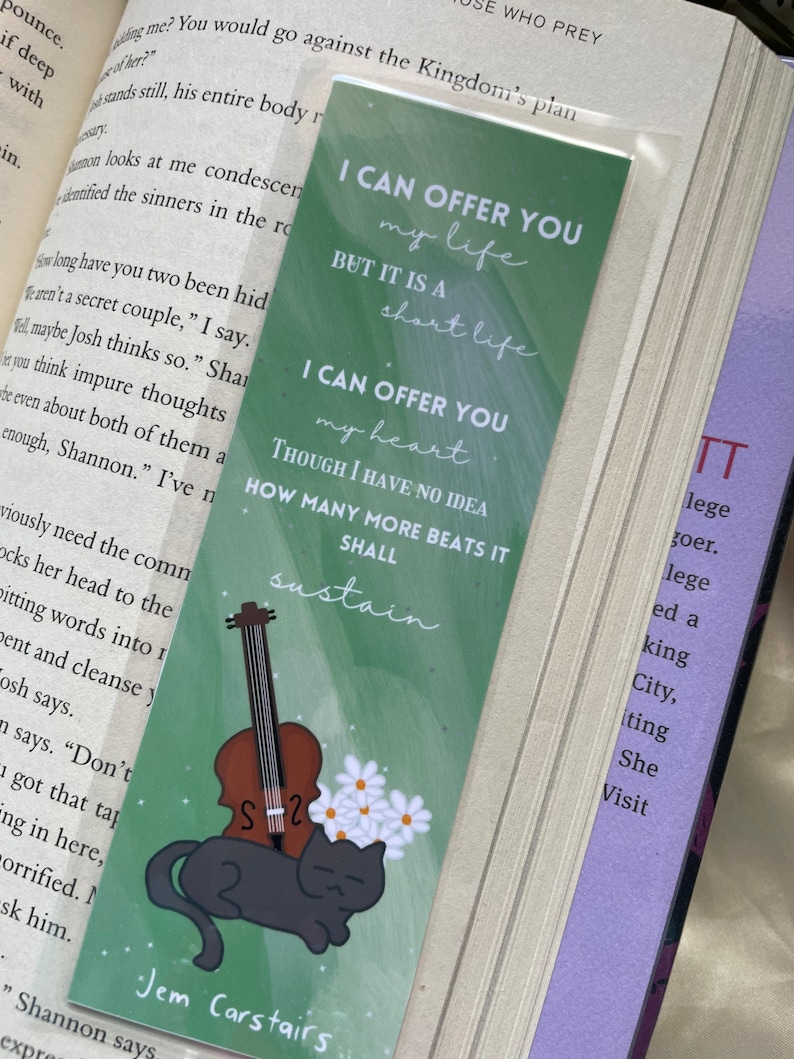 May include: A green bookmark with a black cat and a violin. The bookmark has the text "I can offer you my life but it is a short life. I can offer you my heart though I have no idea how many more beats it shall sustain." The bookmark also has the text "Jem Carstairs" at the bottom.