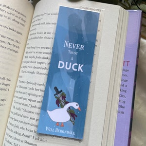 May include: A blue and white bookmark with a white duck and a knife. The bookmark has the text "Never Trust A Duck" and "Will Herondale" on it.