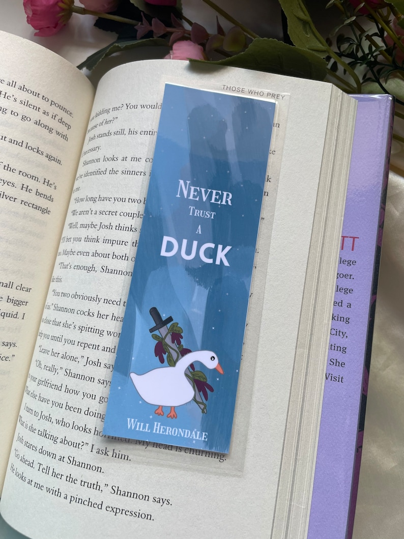May include: A blue and white bookmark with a white duck and a knife. The bookmark has the text "Never Trust A Duck" and "Will Herondale" on it.