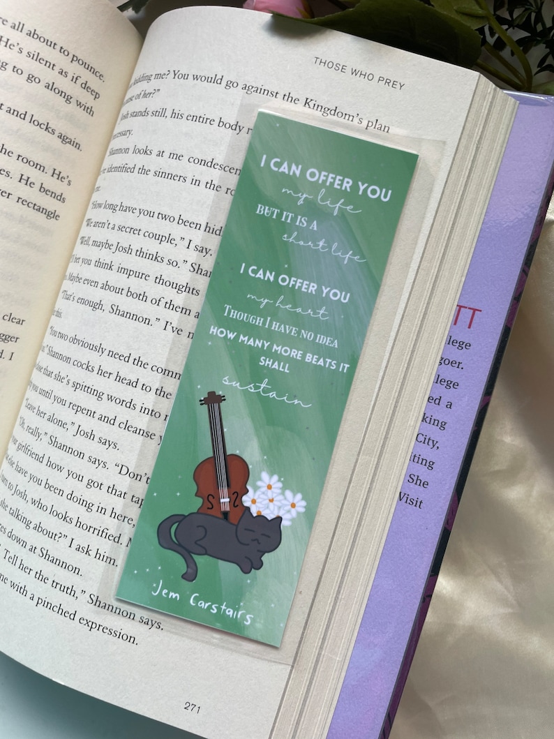May include: Green bookmark with a black cat and a violin. The bookmark has white flowers and the text "I can offer you my life but it is a short life. I can offer you my heart. Though I have no idea how many more beats it shall sustain." The bookmark also has the text "Jem Carstairs" at the bottom.