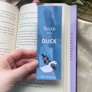 May include: A blue bookmark with a white duck holding a knife. The bookmark has the text "Never Trust A Duck" and "Will Herondale" at the bottom.
