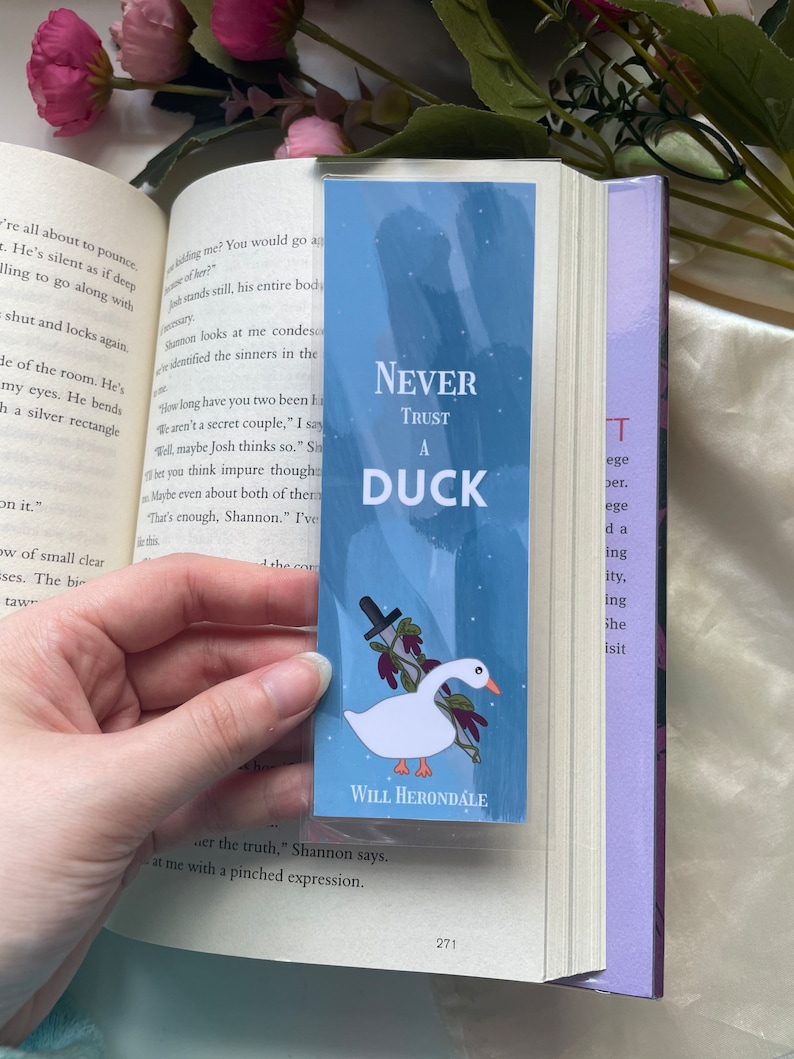 May include: A blue bookmark with a white duck holding a knife. The bookmark has the text "Never Trust A Duck" and "Will Herondale" at the bottom.