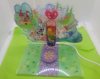 May include: A clear acrylic display stand with a rainbow-colored design and a heart at the top. Two silver earrings with charms are hanging from the stand. The charms are a small mouse and a bee.