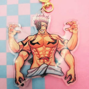 May include: A clear acrylic keychain featuring a muscular anime character with red and black markings, a white mask, and a tongue sticking out. The character has four arms and is in a dynamic pose.