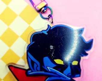 May include: A blue and black cartoon character keychain with a red and blue background. The keychain is made of clear acrylic and has a metal clasp.