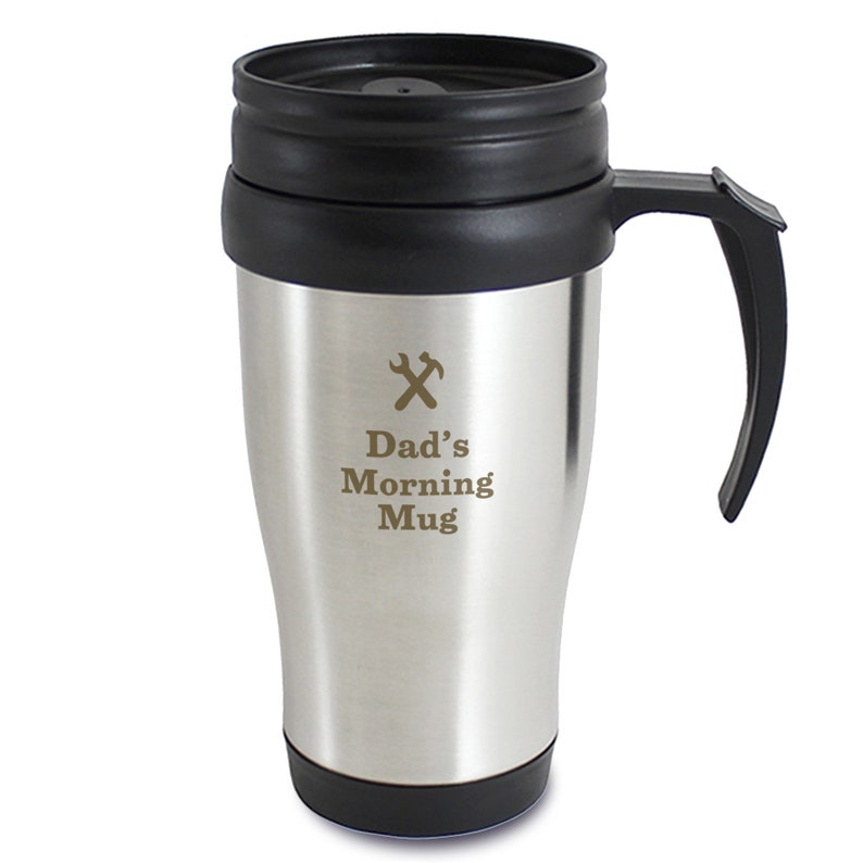 May include: Stainless steel travel mug with a black lid and handle. The mug has an inscription that reads "Dad's Morning Mug" with a wrench and hammer symbol above the text.