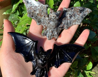 May include: Two carved bat figurines. One is black obsidian and the other is a speckled gray and white stone.