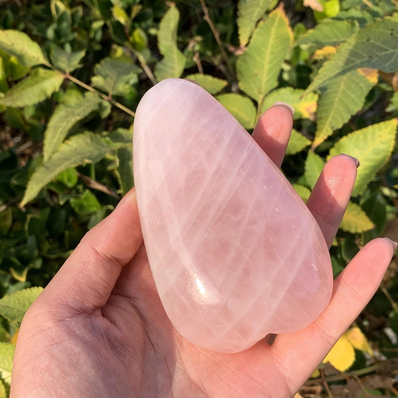 May include: A large, heart-shaped, polished rose quartz crystal with a pale pink color and white striations.