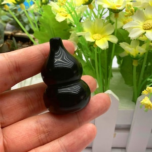 May include: A black polished gourd-shaped pendant made of obsidian. The pendant is smooth and shiny, with a rounded shape and a small hole at the top for hanging.