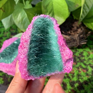 May include: A pink and green crystal with a green, fibrous, sparkly interior. The crystal is shaped like a heart and has a rough, textured exterior.