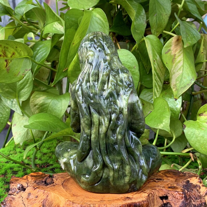 Puede incluir: Una escultura de jade verde de una mujer sentada con las piernas cruzadas y las manos en el regazo. Su cabello es largo y fluido, y su rostro es sereno.