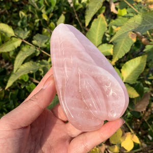 May include: A carved pink rose quartz crystal in the shape of a heart. The crystal is smooth and polished, with a delicate floral design.