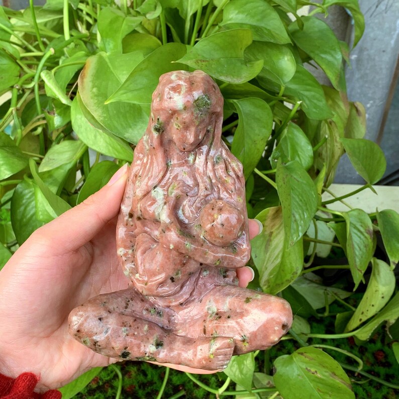 May include: A hand-carved pink and green stone sculpture of a mother and child. The sculpture is made of a type of stone that has a speckled appearance.