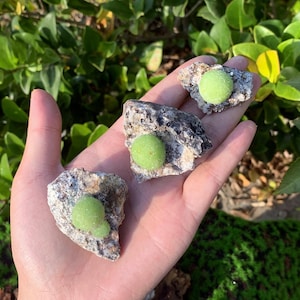 May include: Three small green and white gemstone spheres encased in rough gray rock. The spheres are about 1 inch in diameter.