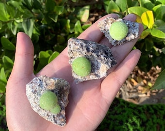 Könnte beinhalten: Drei kleine grüne und weiße Edelsteinkugeln, die in grobem grauem Gestein eingebettet sind. Die Kugeln haben einen Durchmesser von etwa 2,5 cm.