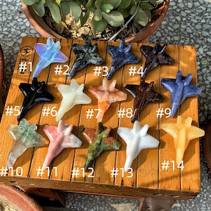 Pode incluir: Quatorze pequenos aviões de pedra preciosa talhados, numerados de 1 a 14, dispostos em duas filas sobre uma superfície de madeira. Os aviões são feitos de vários tipos de pedras preciosas, incluindo ametista, ágata e jaspe.