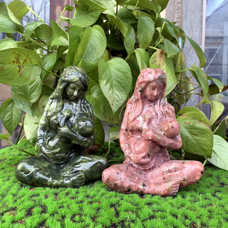 Puede incluir: Dos esculturas de piedra talladas a mano que representan a una madre sosteniendo a un ni&ntilde;o. La escultura de la izquierda es verde y la de la derecha es rosa.
