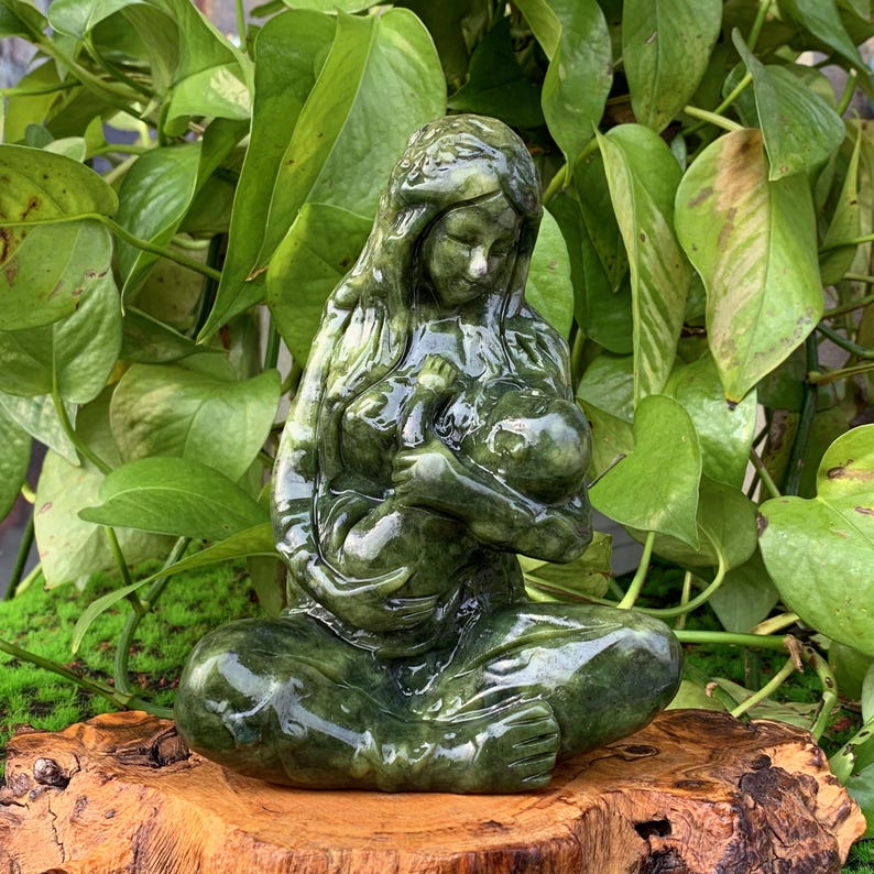 Puede incluir: Una escultura de jade verde de una madre sosteniendo un beb&eacute;. La escultura est&aacute; tallada en un estilo realista y representa a la madre acunando al beb&eacute; en sus brazos.
