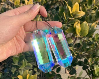 Op de afbeelding: Twee regenboogkleurige kristallen prisma's met een facetgeslepen ontwerp, elk hangend aan een zwart touwtje.