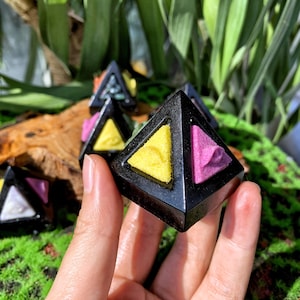 May include: Black obsidian pyramid with three smaller pyramids inside. The smaller pyramids are yellow, pink, and green.