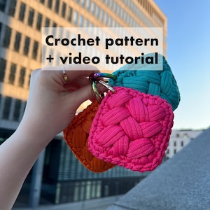 Peut inclure: Trois porte-clés en crochet de couleur rose, turquoise et orange. Les porte-clés sont de forme carrée et présentent un motif tressé. Les porte-clés sont attachés à un anneau de clé argenté.