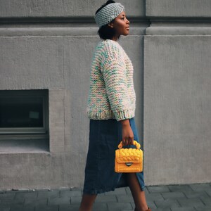 Puede incluir: Una diadema de punto azul claro, un su&eacute;ter de punto grueso en hilo multicolor pastel, una falda midi de mezclilla azul oscuro, botines de gamuza marr&oacute;n con cremalleras laterales y un bolso de ganchillo amarillo brillante con asa trenzada.