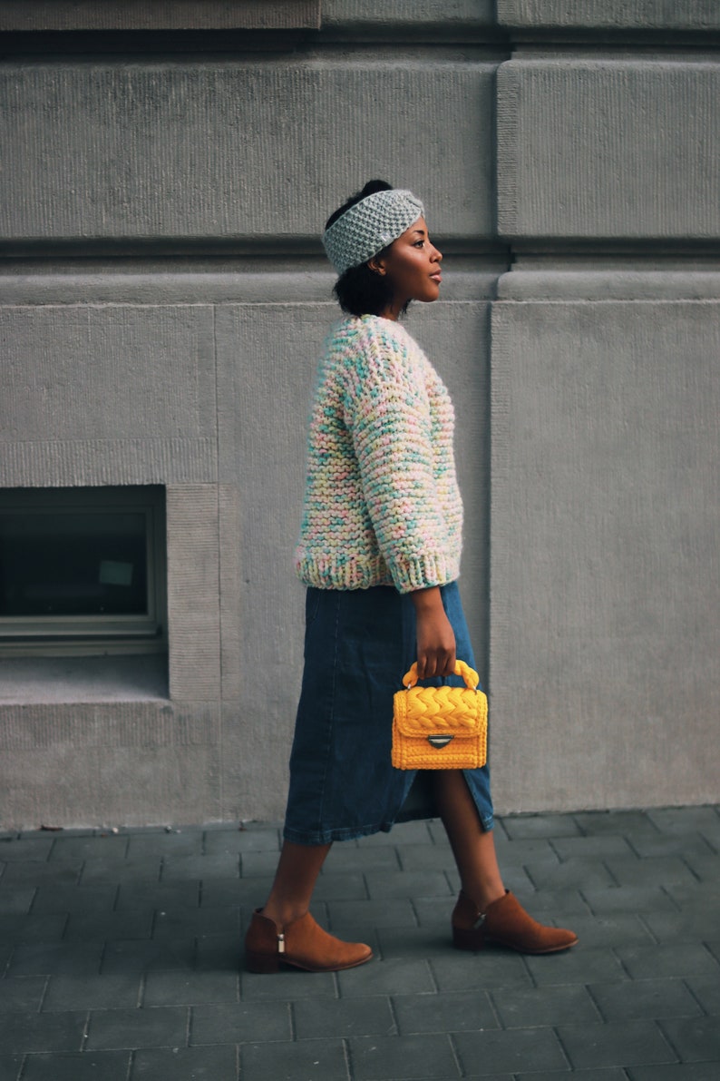 Puede incluir: Una diadema de punto azul claro, un su&eacute;ter de punto grueso en hilo multicolor pastel, una falda midi de mezclilla azul oscuro, botines de gamuza marr&oacute;n con cremalleras laterales y un bolso de ganchillo amarillo brillante con asa trenzada.