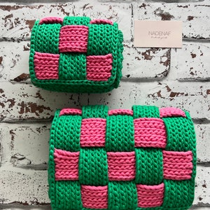 May include: Two rectangular bags crafted from thick, woven yarn in a vibrant checkerboard pattern of bright green and hot pink. The bags feature a chunky, textured knit construction with a folded flap design. A small rectangular card reads NADENAF.