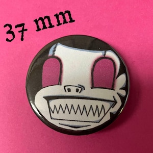 Puede incluir: Un botón de 37 mm con un personaje de dibujos animados con una cara blanca, ojos rosas y una boca en blanco y negro. El personaje tiene una apariencia cosida y un fondo negro.