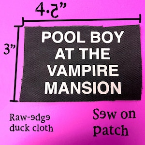 Może przedstawiać: Czarna prostokątna naszywka o szerokości 10,7 cm i wysokości 7,6 cm, z białym napisem „POOL BOY AT THE VAMPIRE MANSION”. Naszywka wykonana jest z surowego płótna kaczkowego i jest naszywką do przyszycia.