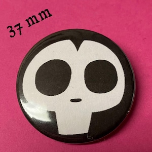 May include: A black and white button with a cartoon skull face. The button is 37 mm in diameter.