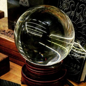 May include: A clear glass sphere, also known as a crystal ball, sits on a dark wood base. The sphere is reflecting light, creating a rainbow effect.