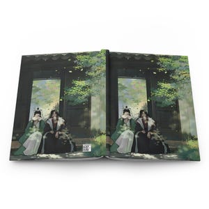 Puede incluir: Diario abierto con una ilustración de dos figuras con vestimenta tradicional, sentadas frente a una estructura de madera oscura con follaje. Las figuras están parcialmente ocultas por abanicos. La portada del diario muestra un diseño artístico detallado.