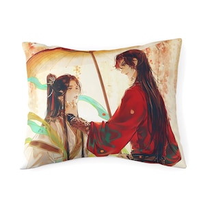May include: A rectangular throw pillow featuring an illustration of two figures under a yellow umbrella. One figure wears a white robe with green accents, while the other wears a red robe. Both have long dark hair and are depicted in a soft art style.