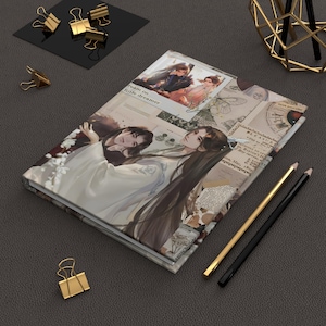 Puede incluir: Un diario de tapa dura con un diseño de collage que presenta ilustraciones de dos personas con ropa tradicional. El diario tiene el texto "dream on little dreamer" y está acompañado de lápices y clips dorados y negros.