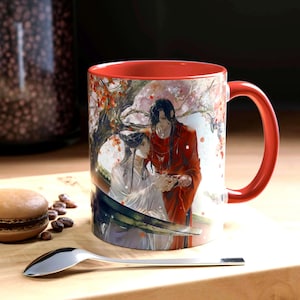 May include: A ceramic mug with a bright red interior and handle, featuring a detailed illustration of two figures in traditional robes under a flowering tree. One figure wears white, the other wears red, and they are shown in a close, intimate pose.