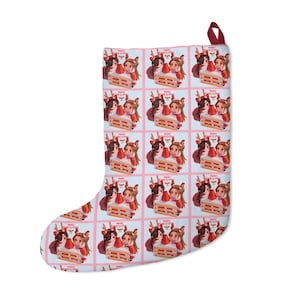 May include: Christmas stocking with a repeating pattern of illustrations. Each illustration features three girls with a cake and the text "Merry Christmas". The stocking has a red loop.