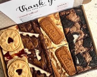 May include: A box of assorted brownie squares. The brownies are topped with various treats, including Oreos, biscuits, and white chocolate. The box is lined with white paper and has a thank you note on top.