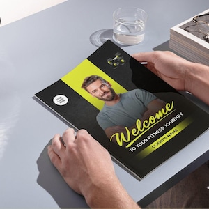 Może przedstawiać: Broszura fitness z czarno-ż&oacute;łtym designem, trzymana przez osobę. Okładka zawiera zdjęcie mężczyzny i słowo "Welcome" w ozdobnej czcionce. Widoczny jest r&oacute;wnież tekst "TO YOUR FITNESS JOURNEY" i "CLIENT'S NAME".